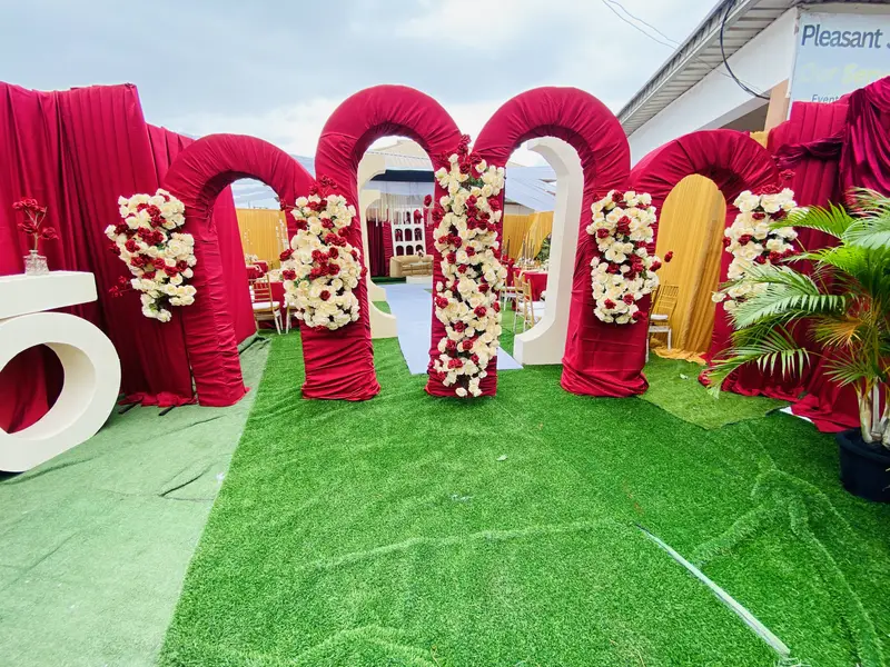 Grand birthday entrance feature with four crimson velvet arches adorned with red and white roses on green lawn