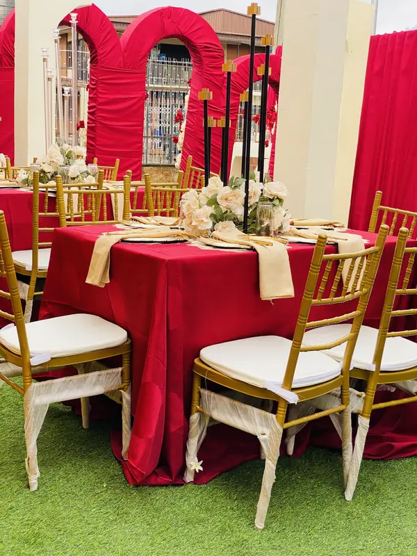Birthday table setting with red linen, gold chairs, champagne napkins and black candelabra against draped arches