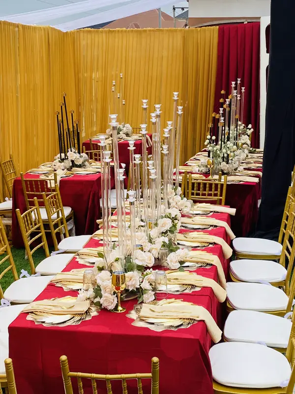 Long birthday dining table styled with crimson linens, gold chairs, towering crystal candelabras and gold drapery
