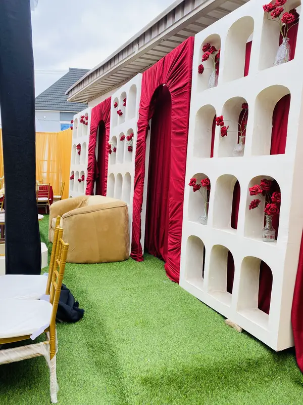 Outdoor birthday stage backdrop with arched floral niches, red drapery and gold armchair