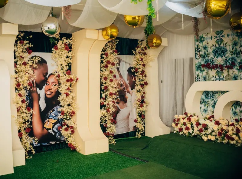 Statement wedding photo gallery walkway featuring large framed couple portraits framed in cascading floral arches, suspended gold mirror spheres, and white ceiling draping