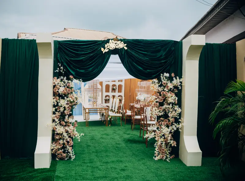 Luxury wedding entrance archway styled with emerald green velvet drapes, cascading blush and cream floral arrangements, and gold monogram crest by Pleasant Jay Events